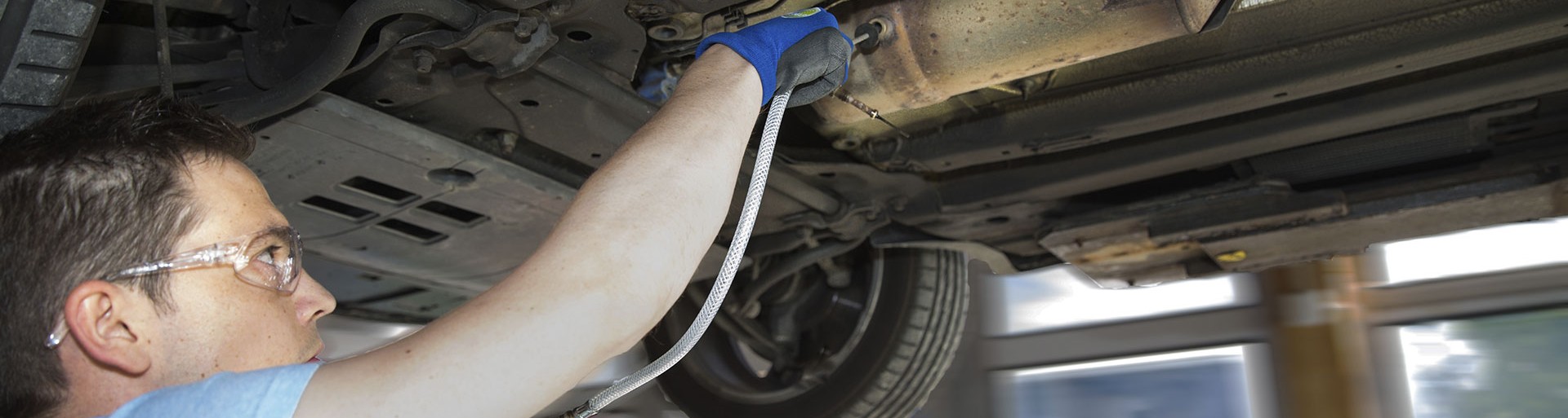 Mechanic under a lifted car using a cup gun with hose and probe to clean a diesel particulate filter