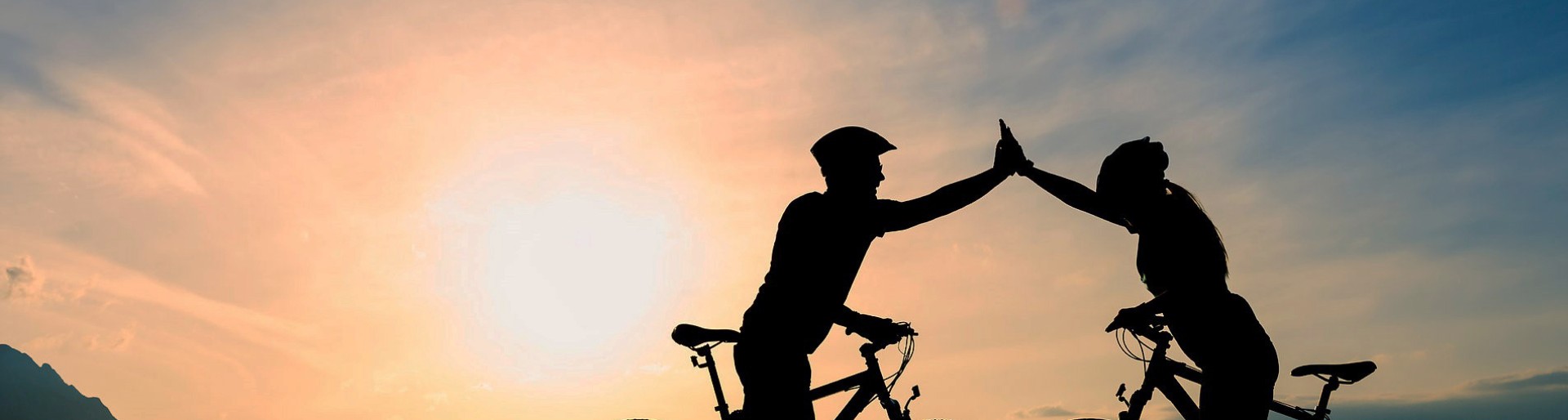 Two cyclists with raised arms with light shining towards the viewer